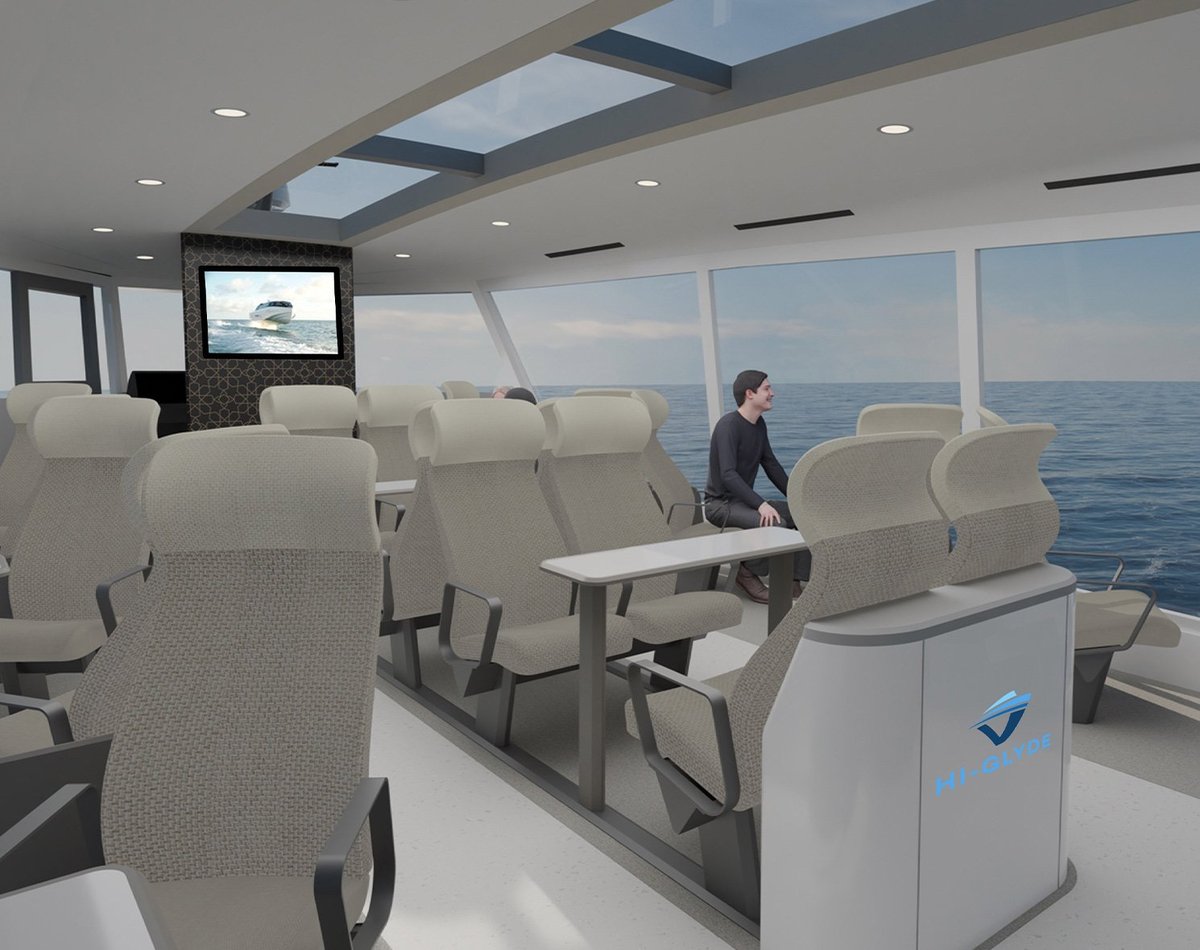 Modern ferry interior with cream seating, large ocean-view windows, skylights, a person standing in the cabin, and a mounted monitor